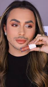Belonger com make em tons quentes segurando batom nude da Belong Be